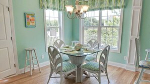 A dining area with a round glass table, white chairs, and a chandelier. - 4 Bedroom, 2.5 Bath,  sleeps 8,  Ocean View, Large Family Room and Sunroom (Emerald Isle)