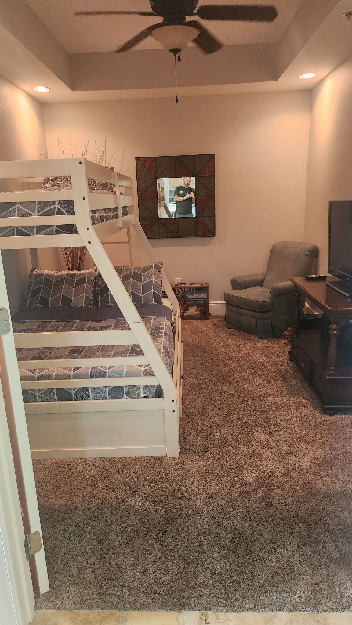 Een kamer met een stapelbed, een stoel, een televisie en een plafondventilator.