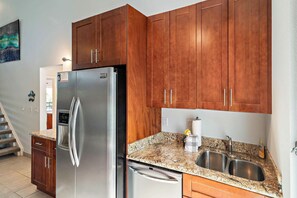 A kitchen with wooden cabinets, a stainless steel refrigerator, granite countertops, and a double sink. - Maui Hill 70 - Spacious 3BR/3BA for 8, 2 King Suites, 3 Lanais, Pool, Near Beach (Kihei)