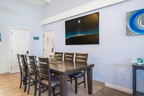 A dining area with a table and chairs, a painting of a night sky, and a sign on the wall. - Maui Hill 70 - Spacious 3BR/3BA for 8, 2 King Suites, 3 Lanais, Pool, Near Beach (Kihei)