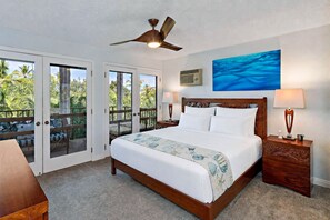 A hotel room with a bed, two bedside tables, a ceiling fan, a painting, and a view through the glass doors. - Maui Hill 70 - Spacious 3BR/3BA for 8, 2 King Suites, 3 Lanais, Pool, Near Beach (Kihei)