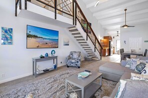 Ein geräumiges Wohnzimmer mit einem großen Gemälde, einer Treppe und Blick zur Küche.