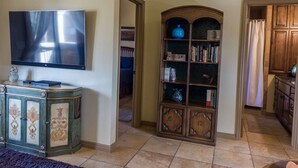 A living room with a flat-screen TV, a decorative cabinet, and a bookshelf. - The Desert Hideaway, Small place, big adventures (St George)