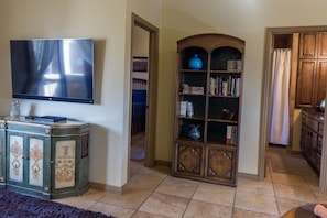 A living room with a flat-screen TV, a decorative cabinet, and a bookshelf. - The Desert Hideaway, Small place, big adventures (St George)