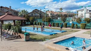 A swimming pool area with lounge chairs, a small building, and a fenced tennis court. - The Desert Hideaway, Small place, big adventures (St George)