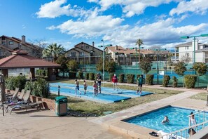 A swimming pool area with lounge chairs, a small building, and a fenced tennis court. - The Desert Hideaway, Small place, big adventures (St George)