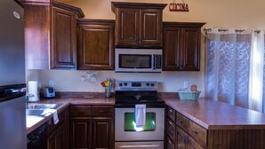A kitchen with wooden cabinets, a microwave, a stove, and a sink. - The Desert Hideaway, Small place, big adventures (St George)