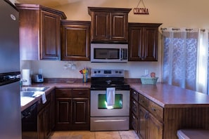 A kitchen with wooden cabinets, a microwave, a stove, and a sink. - The Desert Hideaway, Small place, big adventures (St George)