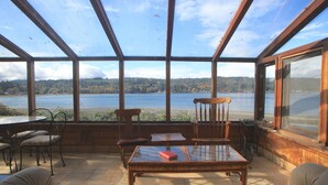 Une véranda dotée d’une grande baie vitrée donnant sur un lac, et aménagée avec une table, des chaises et un canapé.