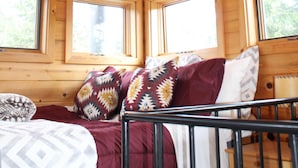 Interior de una cabaña de madera con cama, almohadas y una ventana.