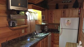 A compact kitchen with wooden cabinets, a granite countertop, a microwave, a stove, and a refrigerator. - Mountain serenity close to hiking, rafting, fishing and kayaking.  "Coyote Song" (Topton)