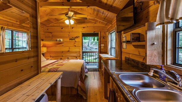A cabin interior with a wooden interior, a dining table, a kitchen with a sink, and a ceiling fan. - Mountain serenity close to hiking, rafting, fishing and kayaking.  "Coyote Song" (Topton)
