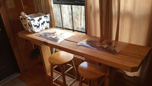A wooden table with two stools, a window with curtains, and a bag with a deer pattern. - Mountain serenity close to hiking, rafting, fishing and kayaking.  "Coyote Song" (Topton)