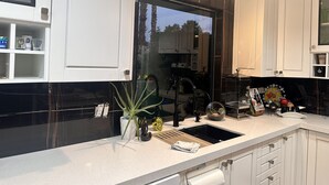 Cozinha moderna com armários brancos, painel de fundo preto e janela com vista para palmeiras.
