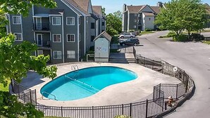 A residential area with a swimming pool surrounded by a fence, a small utility building, and multi-story apartment buildings in the background. - Everyone Welcome! Private WiFi, Heated Pool, Gas Grills, Catch the View! (Gatlinburg)