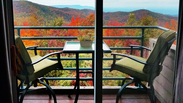 A balcony with two chairs and a table, overlooking a scenic view of autumn foliage and distant mountains. - Everyone Welcome! Private WiFi, Heated Pool, Gas Grills, Catch the View! (Gatlinburg)
