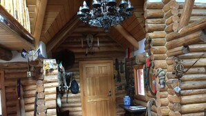 Et interieur i en træhytte med en trädør, en lysekrone og forskellige dekorationer, herunder flag og et ur.