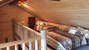 A wooden cabin bedroom with a sloped ceiling, a wooden staircase, and a bed with patterned bedding. - Make your reservation fast as inquiries are coming in daily.  (Redford)