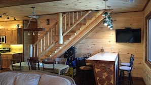 A cozy cabin interior with a wooden staircase, a dining area, and a bar with stools. - Make your reservation fast as inquiries are coming in daily.  (Redford)