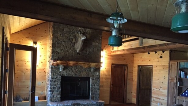 A rustic cabin interior with a stone fireplace, wooden walls, and a cozy seating area. - Make your reservation fast as inquiries are coming in daily.  (Redford)