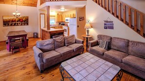 A cozy living room with a wooden floor, two sofas, a coffee table, and a staircase leading to a kitchen. - Amazing Cabin w/Firepit, Gametable, Hot Tub, Wifi, Cable (Banner Elk)