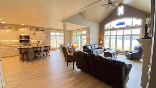 A spacious living area with a large sofa, a dining table, and a kitchen in the background. - Waterfront Home With Swimming Pond - 61  - 5 star reviews  FREE 2 HOUR PONTOON (Sturgeon Bay)