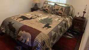 A bed with a quilt featuring animal prints, a bedside lamp, a nightstand with a phone, and framed pictures on the wall.
