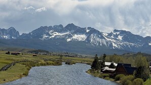 A river flowing through a valley with mountains in the background and a small settlement with houses and a fence.