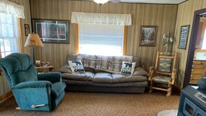 A cozy cabin interior with a sofa, armchair, and a wood-burning stove.