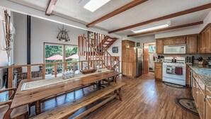 Una cocina amplia con vigas de madera, una mesa grande de madera y una estufa empotrada.