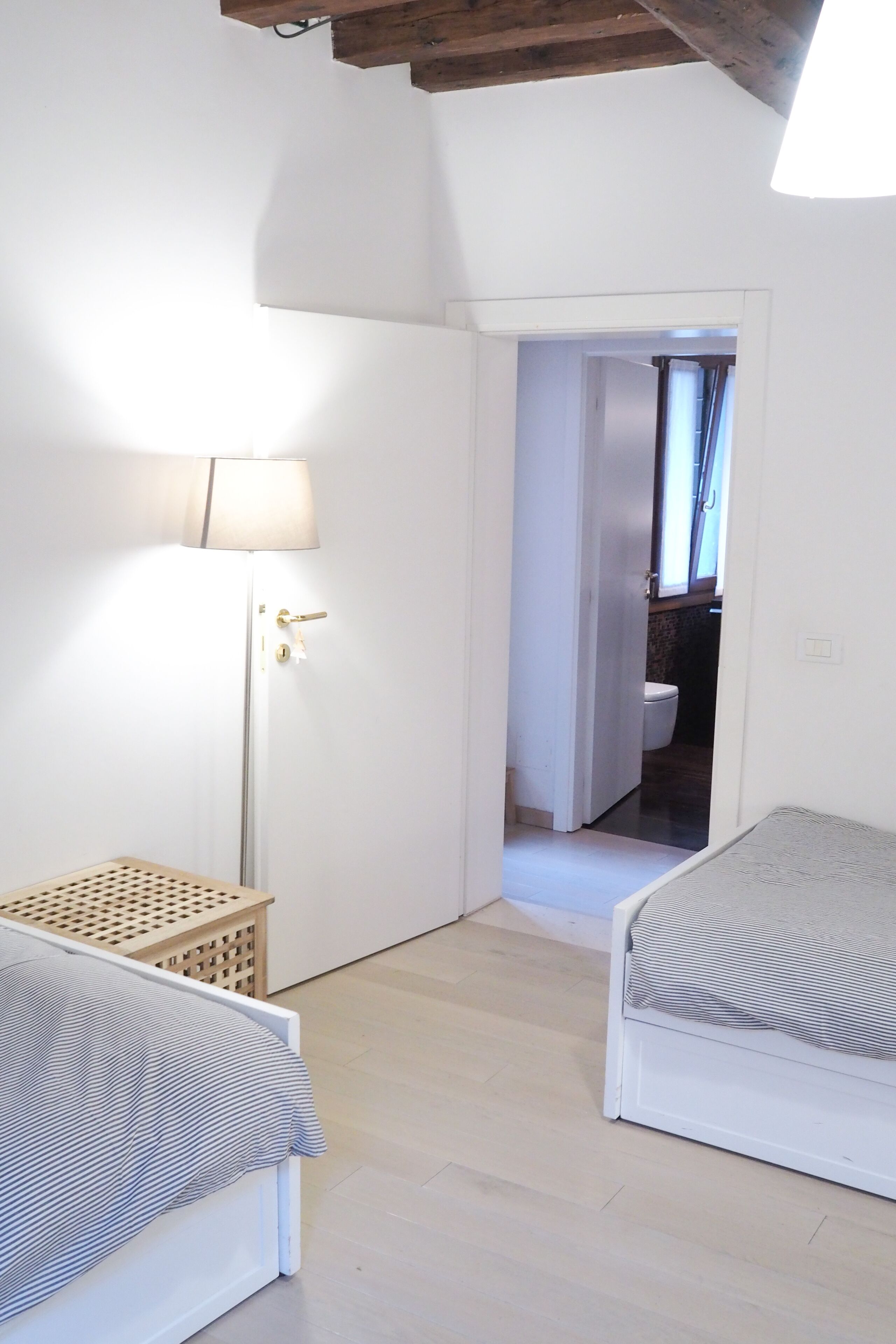 Une chambre avec deux lits, une lampe sur pied et une porte donnant sur une salle de bain.