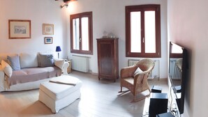 Un salon comprenant un canapé, un pouf, un fauteuil en osier et un téléviseur.