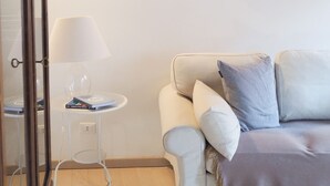 Une pièce chaleureuse avec un canapé blanc, une petite table ronde surmontée d’une lampe et un tableau encadré accroché au mur.