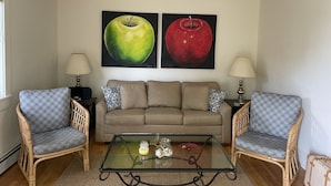 A living room with a beige sofa, two patterned armchairs, a glass coffee table, and two lamps. There are two paintings of apples on the wall. - Charming, 2BR Oceanfront cottage with stunning views.  (Southwest Harbor)
