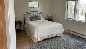 A bedroom with a bed, a window, a nightstand, a lamp, and a rug. - Charming, 2BR Oceanfront cottage with stunning views.  (Southwest Harbor)