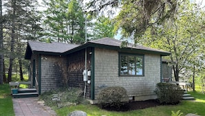 A small, single-story cabin with a sloped roof, a porch with steps, and a mailbox labeled "457A APPLE". - Charming, 2BR Oceanfront cottage with stunning views.  (Southwest Harbor)