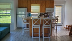 A kitchen with wooden cabinets, a central island with chairs, a refrigerator, a microwave, and a window with blinds. - Bird watching paradise! (Seadrift)