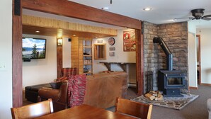 Un salon chaleureux avec une cheminée en pierre, des poutres apparentes et un téléviseur fixé au mur.