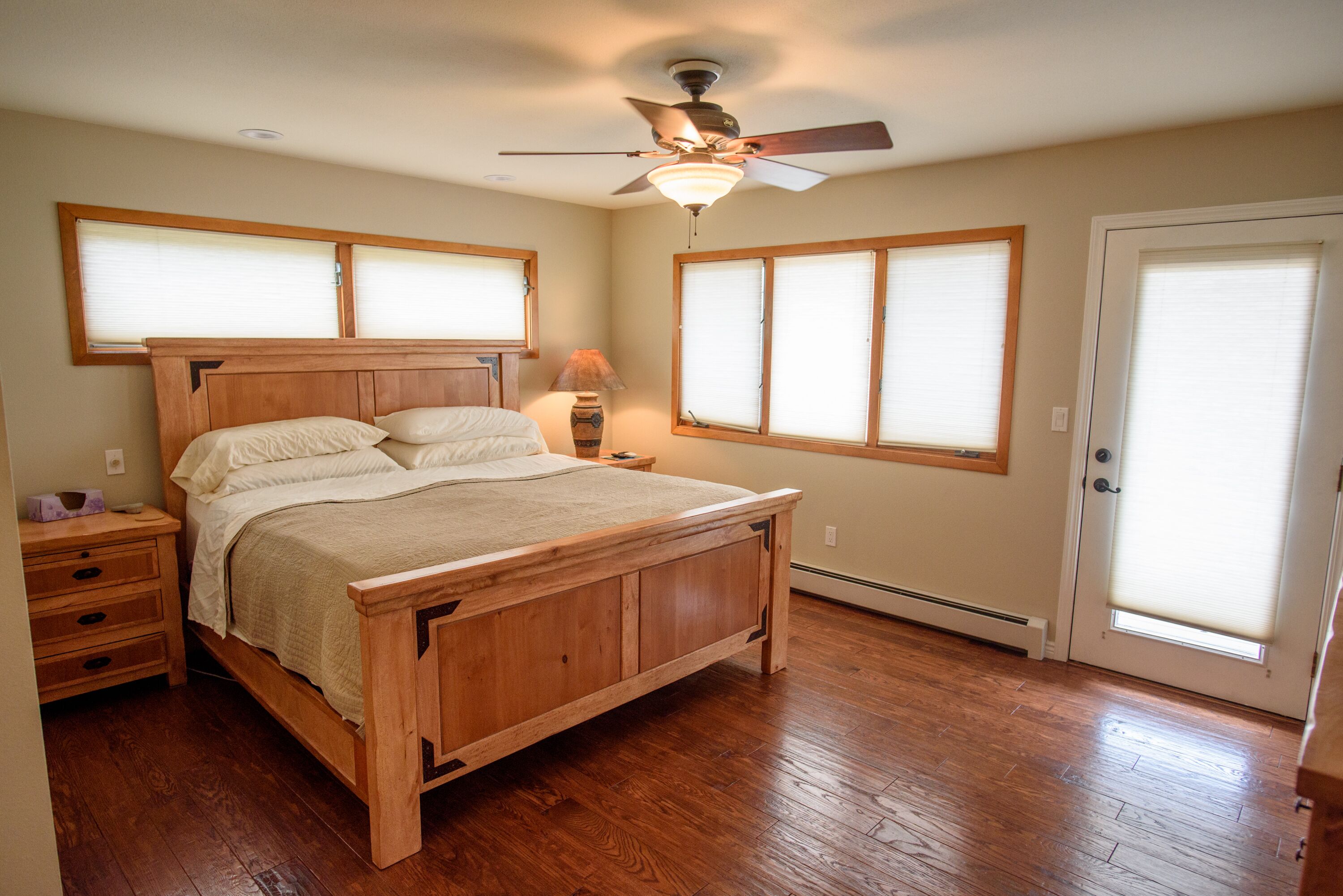 Une chambre avec un lit en bois, un ventilateur de plafond et une fenêtre avec des stores.