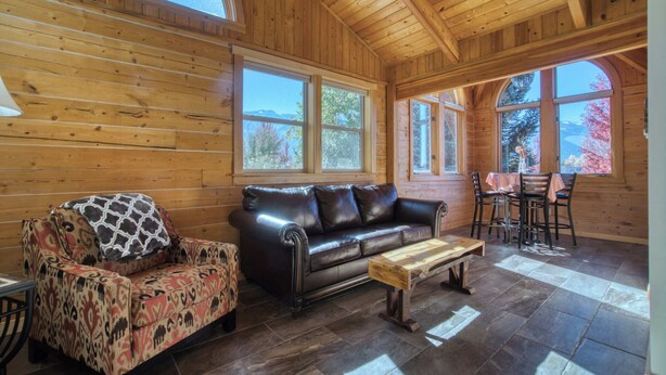 A cozy log cabin interior with a leather sofa, patterned armchair, and a dining table with chairs. - Mt. Joseph Lodge in Downtown Joseph: Unit #7 (Joseph)