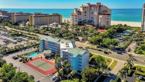 Ett hotell vid kusten med flera byggnader, en parkeringsplats och en tennisbana.