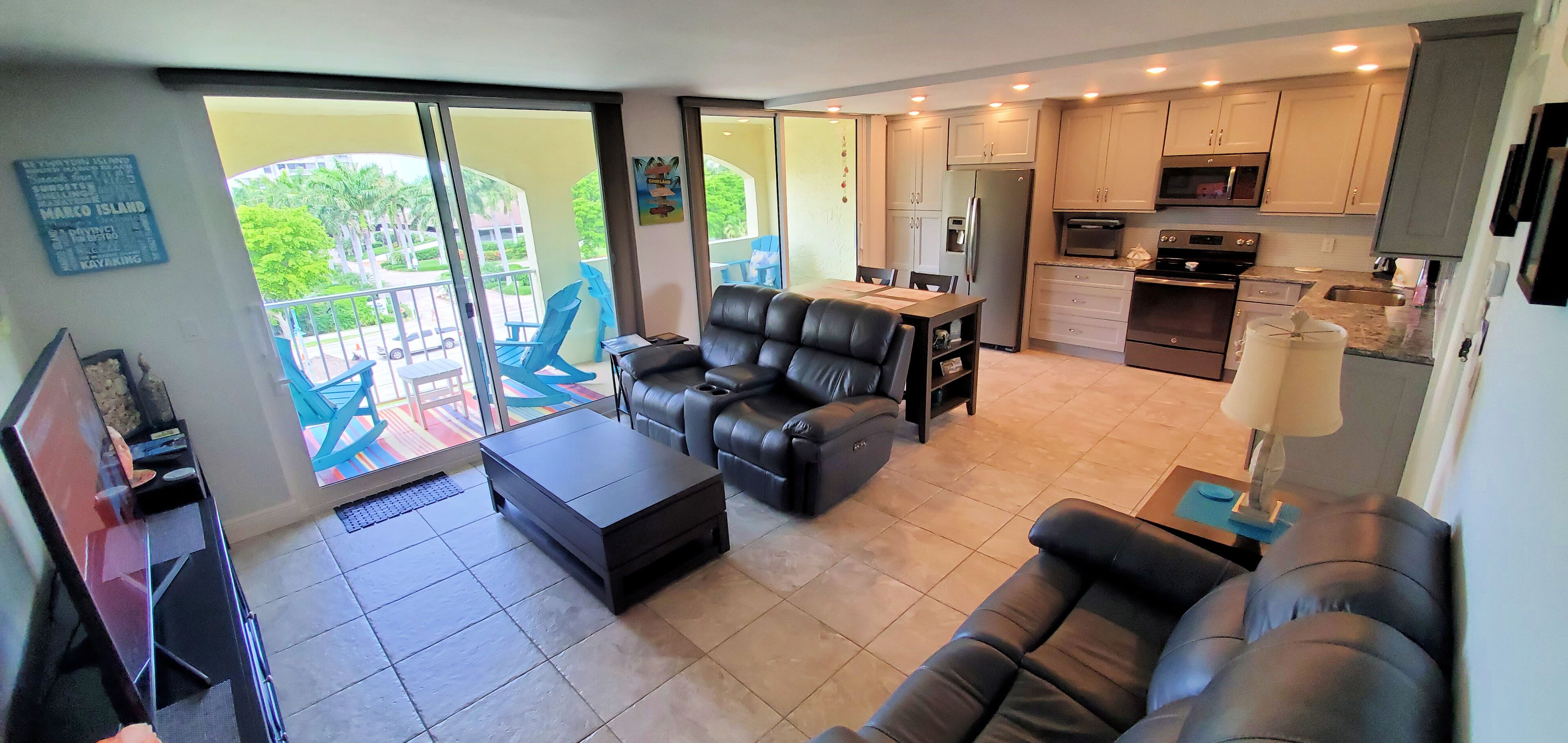 A modern living room with a sofa, a coffee table, and a dining area with chairs. There is a kitchen with cabinets and appliances.