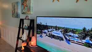 Ett rum med en tv-skärm som visar en strandscen, en hylla med dekorativa föremål och ett tänt ljus.