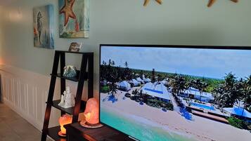 Una habitación con una televisión que muestra una escena de playa, una estantería con objetos decorativos y una vela encendida.