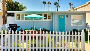 A single-story house with a white picket fence, a blue door, and a small patio with a table and umbrella. -  🏄GREAT LOCATION: FAMILY & PET FRIENDLY BEACH COTTAGE🌊 (San Clemente)