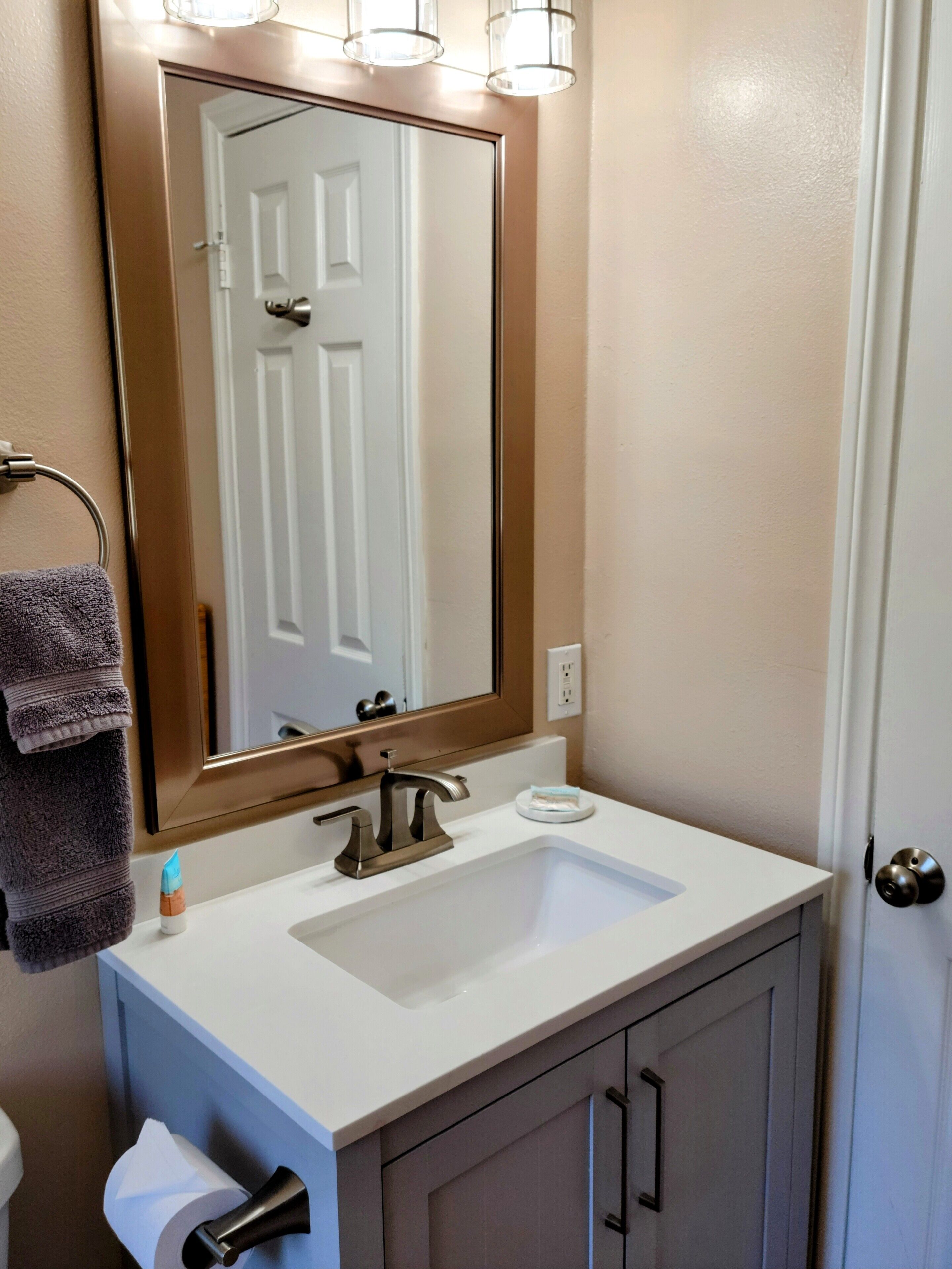 Un baño con un lavamanos blanco, un espejo grande y un perchero para toallas.