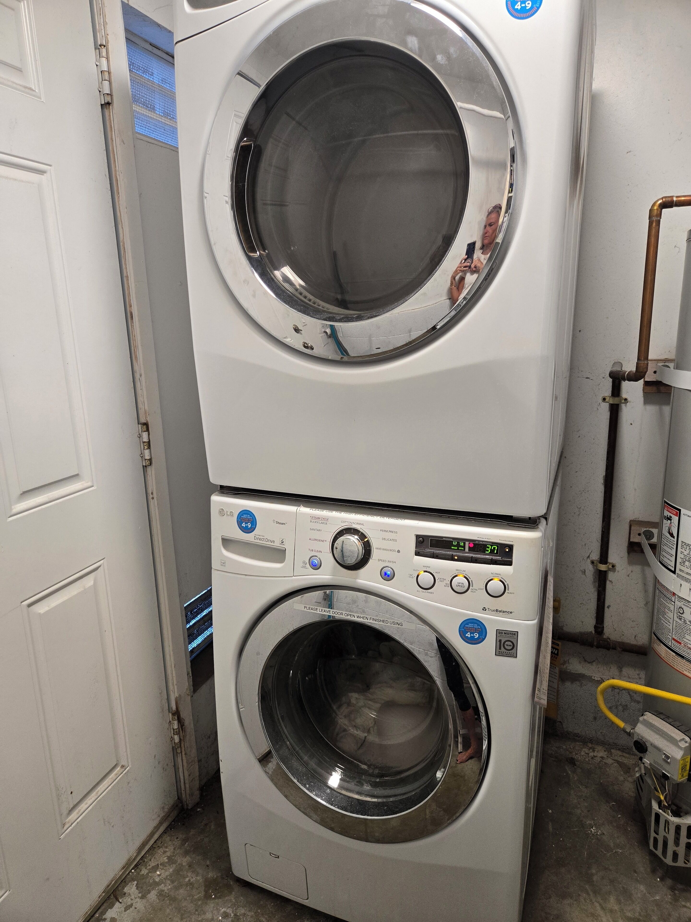 A stacked washer and dryer unit with a digital display, control buttons, and a 'Please leave door open when finished using' sign.