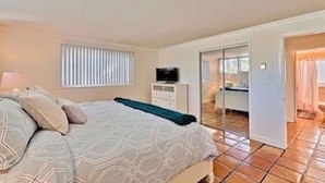 A bedroom with a bed, a TV on a dresser, and a bathroom visible through an open door. -  🏄GREAT LOCATION: FAMILY & PET FRIENDLY BEACH COTTAGE🌊 (San Clemente)