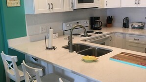 A kitchen with white cabinets, a microwave, a sink, and a bar area with white chairs. -  Gorgeous Gulf Front Condo on 30A! Back Porch Opens to Private Beach (Seacrest)