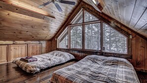 A cabin with two beds, wooden walls, a sloped ceiling, and large windows overlooking a forest. - Yellow Birch Lodge - Private Vacation Rental Home       (Eagle River)